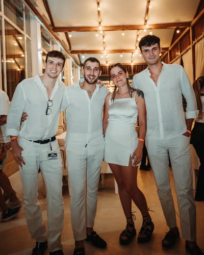 Quattro persone vestite di bianco sorridono in posa dentro un locale con luci calde