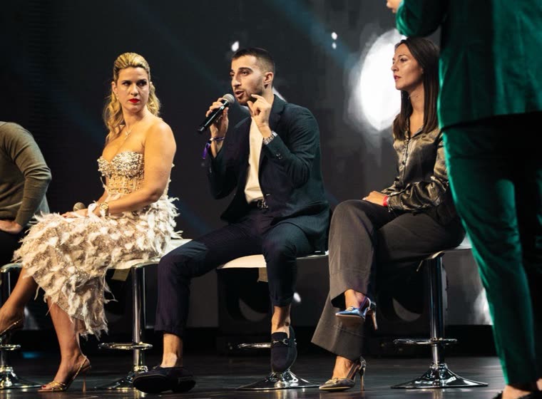 Intervista sul palco di un evento: tre persone sedute e un uomo in abito verde in piedi