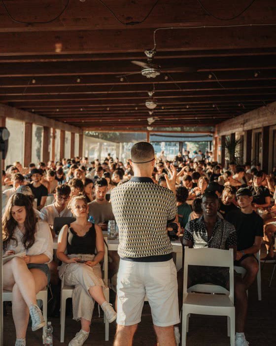 Un relatore in piedi davanti a una sala piena di persone sedute, durante un workshop