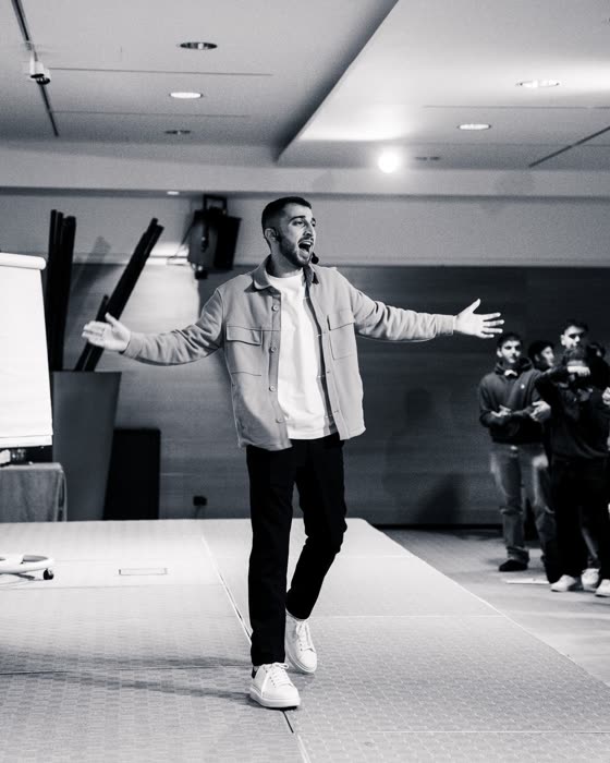 Un relatore a braccia aperte sul palco di una sala conferenze, foto in bianco e nero