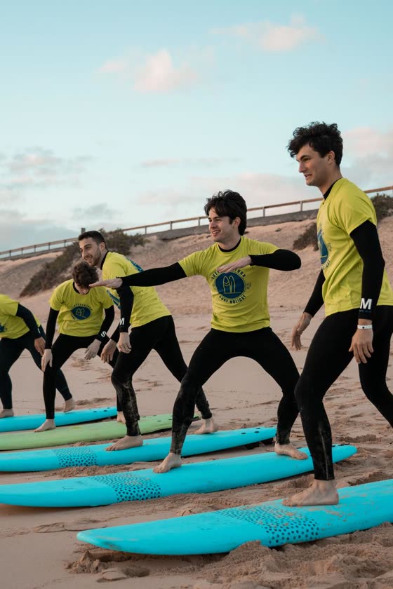 Un gruppo di ragazzi con magliette gialle fa una lezione di surf sulla spiaggia